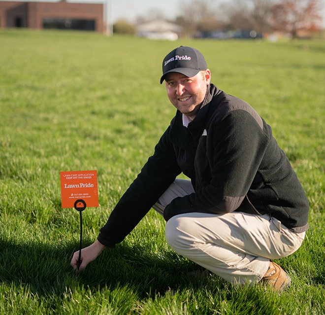 Man sitting on a grassy field with a 'Lawn Pride' board.
