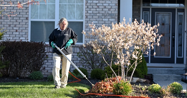 Woman trimming bushes outside of a house.