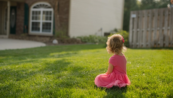 Little girl sitting in the lawn in front of her house
